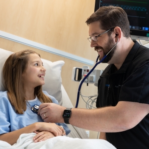 male healthcare worker in blue scrubs caring for girl patient in hospital room