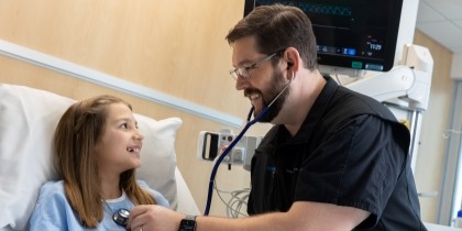 male healthcare worker in blue scrubs caring for girl patient in hospital room