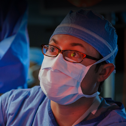 A man in blue scrubs, a cap, and a face mask