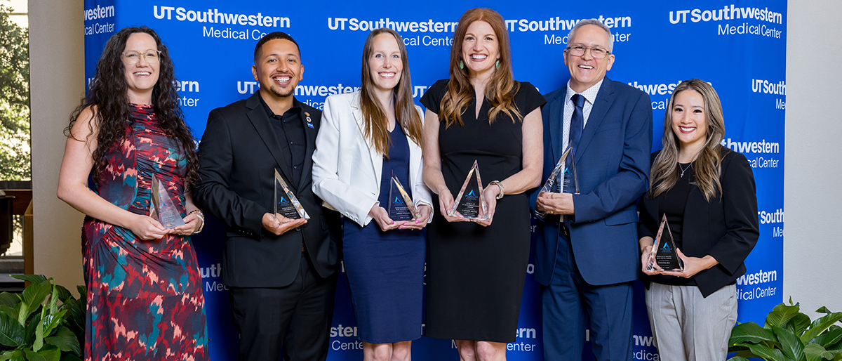 The 6 awardees stand in front of a blue UTSouthwestern Medical Center backdrop, holding their triangular glass awards.