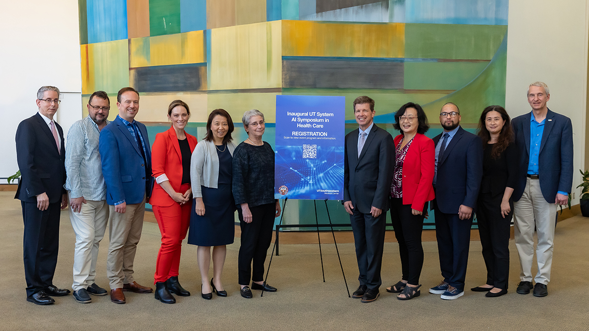 6 men and 5 women gathered in front of a colorful art display with a blue sign on an easle with name of gathering.