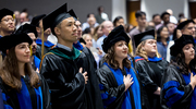 The audience of graduates and faculty rises for the national anthem.