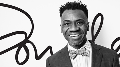 Smiling man dark spiked hair, wearing a dark jacket, striped shirt, and bow tie.