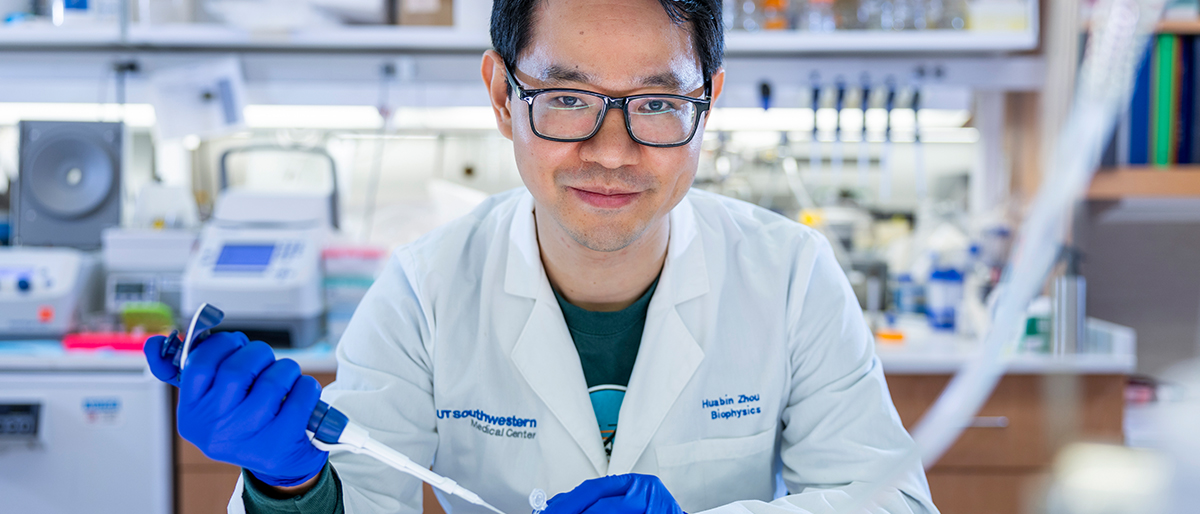 Smiling lab technician holding a test tube and dropper.