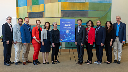 6 men and 5 women gathered in front of a colorful art display with a blue sign on an easle with name of gathering.