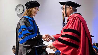 young asian woman in cap and gown receives diploma from UT Southwestern president Dr. Podolsky