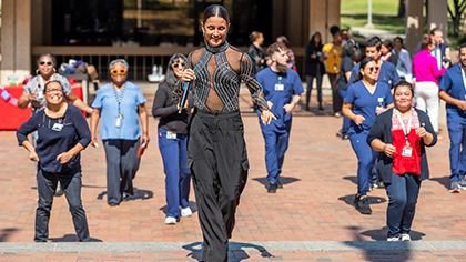 Smiling woman holding a microphone, leading UT Southwestern employees in a dance.