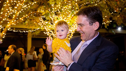 Man holding child in his arms in a courtyard of lit trees