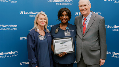 at left, a blond woman in scrubs, a black woman with short hair in scrubs, and (right) older balding man in grey suit and red tie