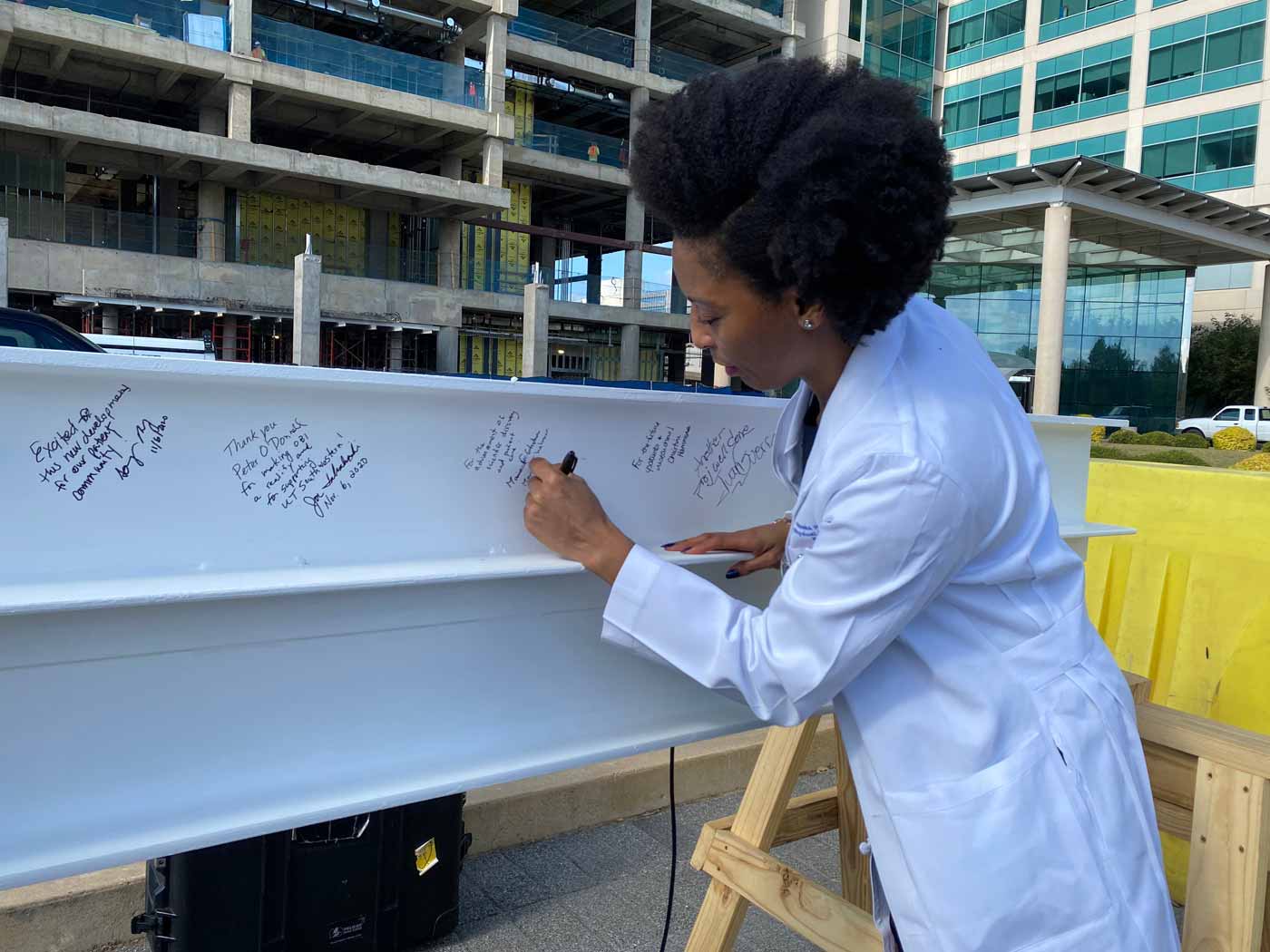 Dr. Nneka Ifejika, Associate Professor of Physical Medicine and Rehabilitation, writes a message on a steel beam. Woman in lab coat signing beam