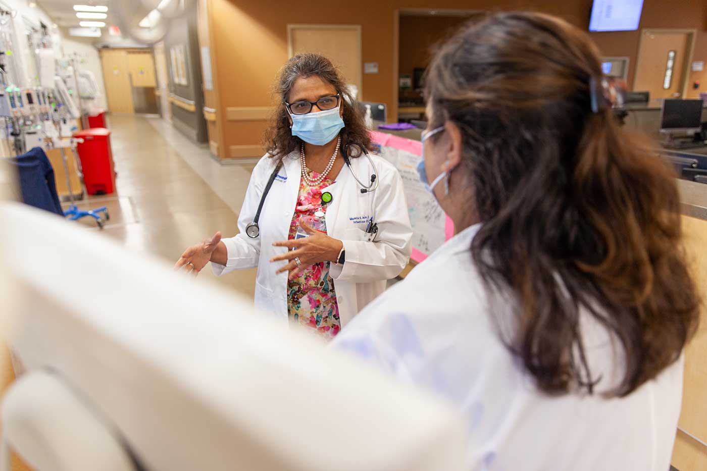 Woman in lab coat speaks to another person in hospital