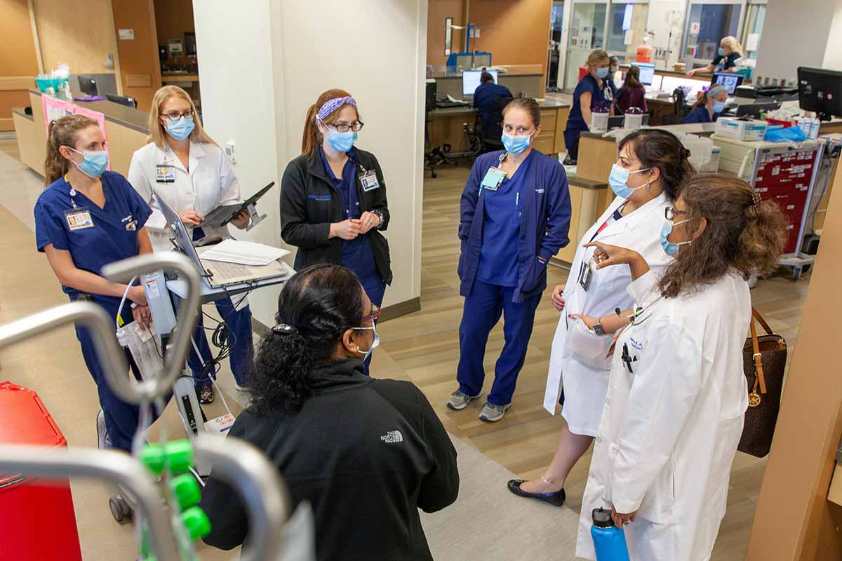Dr. Mamta Jain (right) confers with other team members in the COVID-19 unit at Clements University Hospital. Hospital staff standing in circle