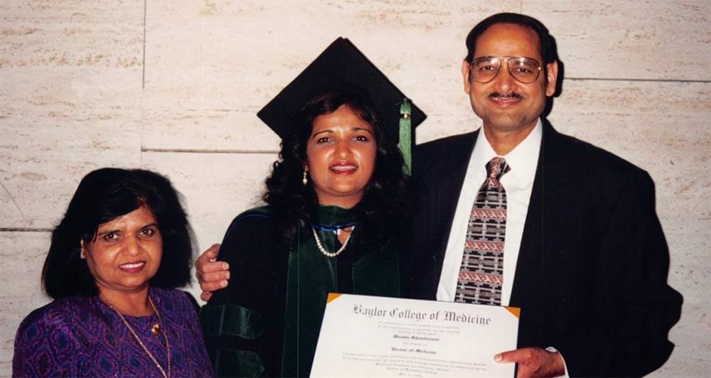 Dr. Jain earned a medical degree in 1996 from Baylor College of Medicine. Her proud parents attended her graduation. Woman in graduation gown with parents, holding diploma