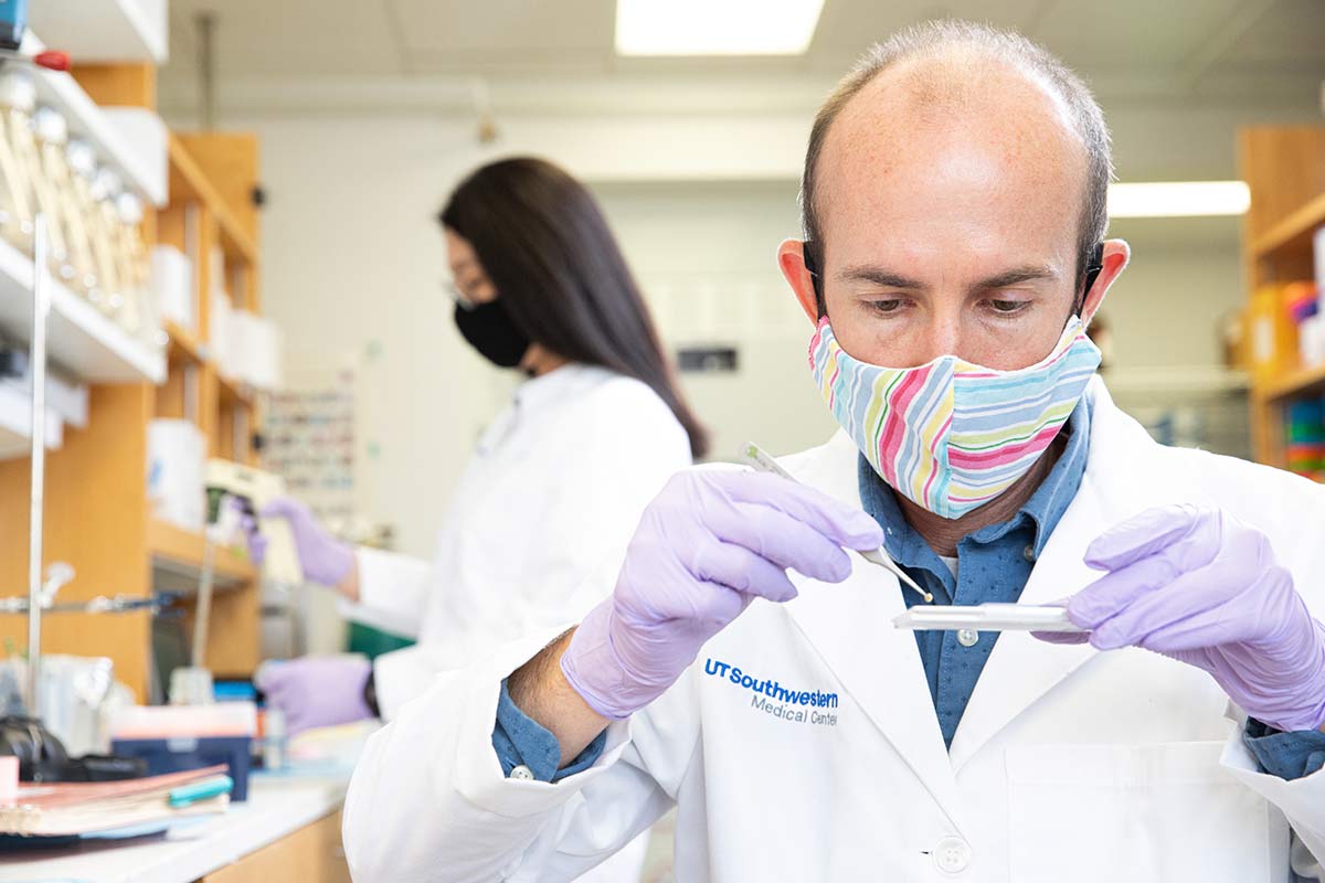 Dr. Ryan Hibbs prepares a sample for structural study by cryo-EM. Man wearing mask in whtie lab coat, working with slide