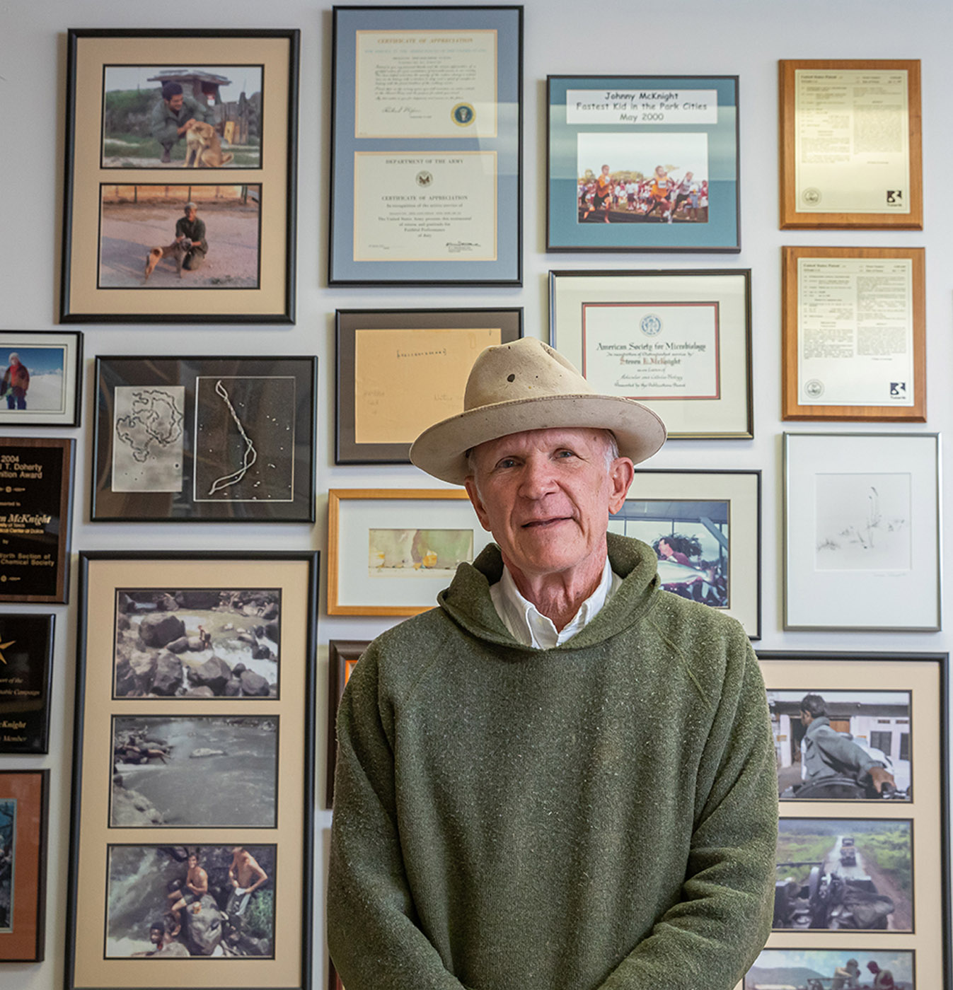Photos from his combat service in Vietnam adorn the walls in Dr. McKnight’s office along with memories of his accomplishments as a scientist. Man in hat sitting in front of photos