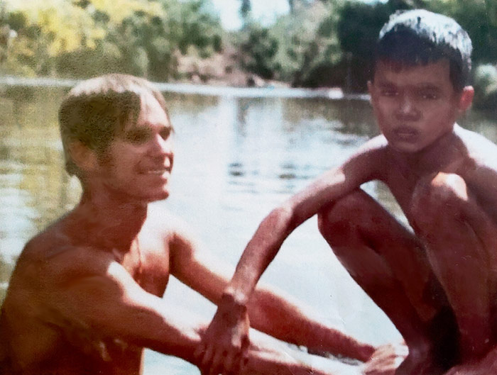 Dr. Steven McKnight, then an enlisted soldier in the Army, interacts with a village child in Vietnam. Man in water next to boy sitting on dock