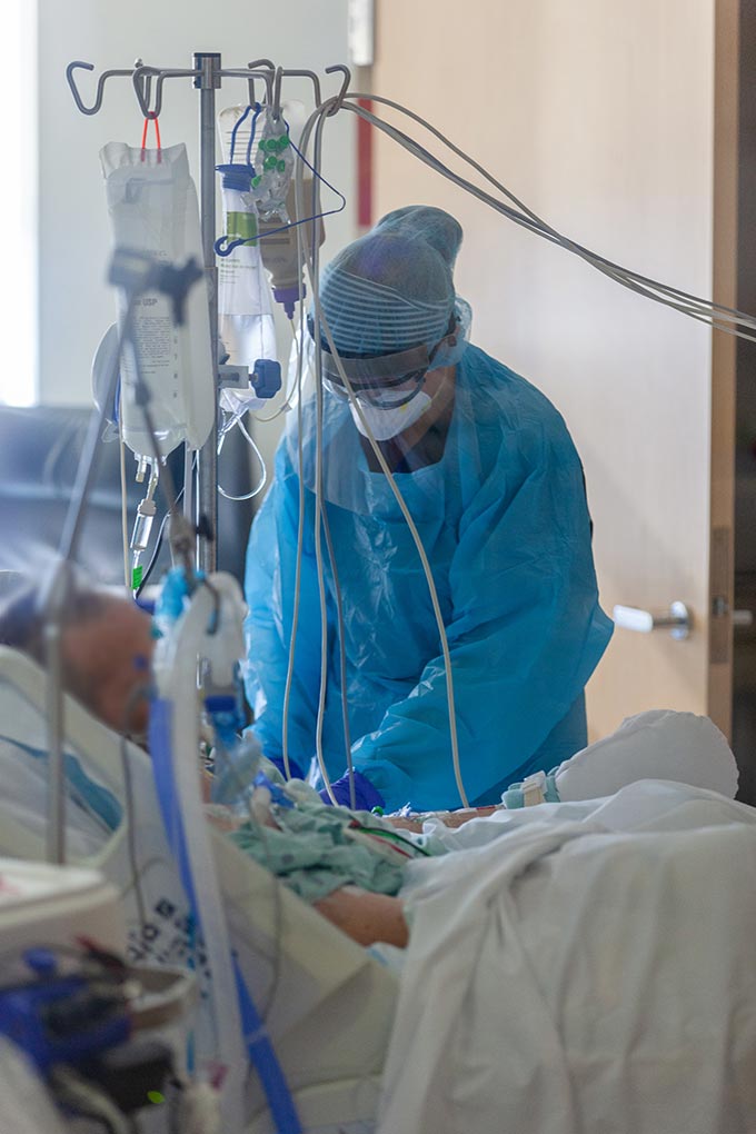 Registered Nurse Rachel Butterfield treats a patient in a designated COVID-19 ward at CUH. Person in mask and scrubs helps patient