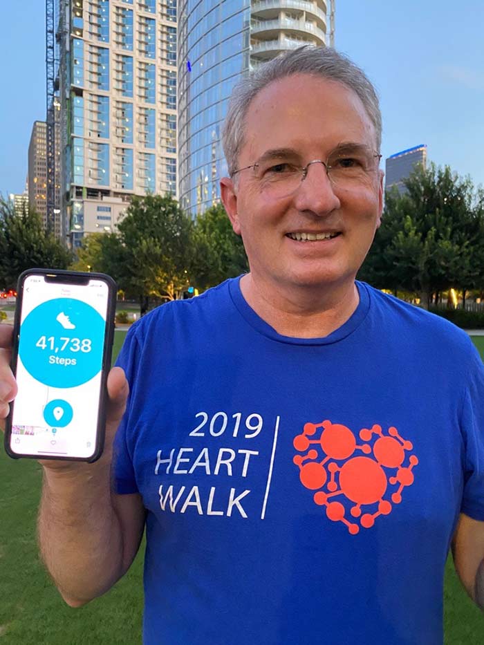 Dr. John Warner, EVP for Health System Affairs, beat his goal of 40,000 steps. Man in blue 2019 heart walk, holding up phone