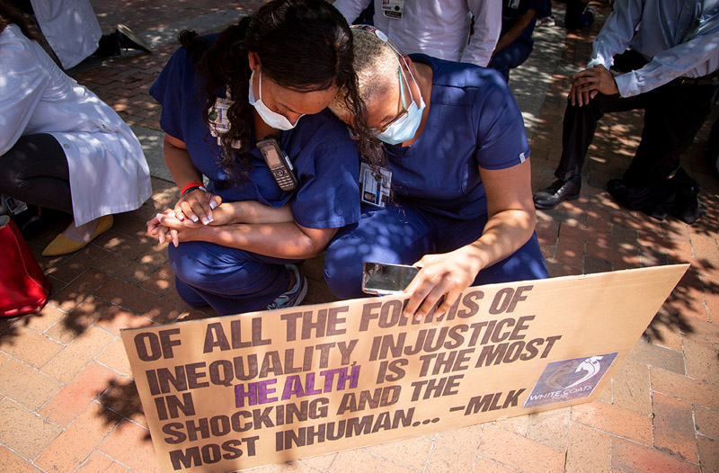 Registered Nurses Filoshia Barrow (left) and Adrianne Johnson comforted each other during the kneeling demonstration. Two women in masks, holding sign and holding hands