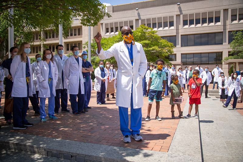 Dr. Dale Okorodudu, Assistant Professor of Internal Medicine, encouraged colleagues to use their influence as physicians to speak up about issues surrounding racial injustice. Black man in scrubs, white lab coat, wearing orange mask, speaking to crowd