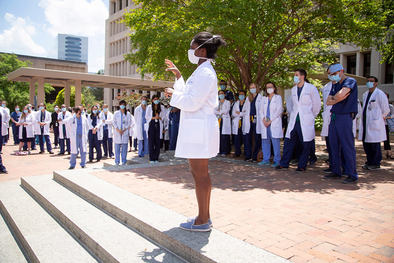 Medical student Louise Atadja gave an impromptu speech to attendees during the rally. Black woman in mask, white coat, speaking to crowd