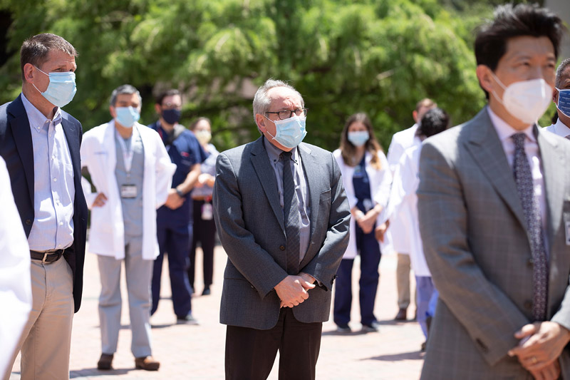 From left: Executive leaders Arnim Dontes, EVP for Business Affairs; President Dr. Daniel K. Podolsky; and Dr. W. P. Andrew Lee, EVP for Academic Affairs, Provost, and Dean of the Medical School People in suits and masks standing and listening amongst crowd of people