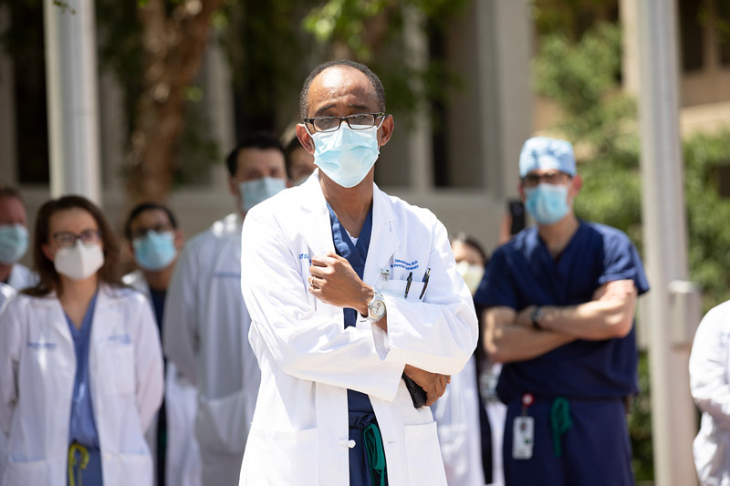 Dr. Mehari Gebreyohanns, Assistant Professor of Neurology and Neurotherapeutics, said addressing racial inequities in other areas of society is relevant at medical institutions because health care and social issues are intimately linked. Black man with glasses, surgical mask, wearing white lab coat over scrubs, speaking