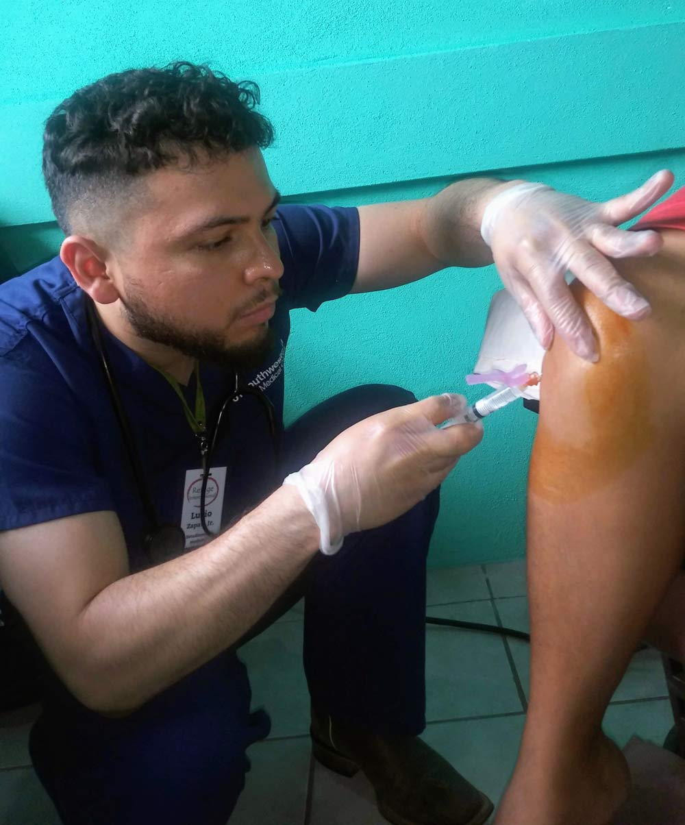 Mr. Zapata delivers a steroid injection to a patient with arthritis during a 2019 medical mission trip in Sarstún, Guatemala with Refuge International. Man injecting person's leg with syringe