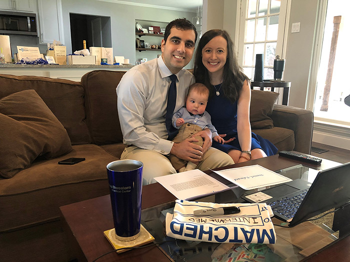 Caption here Two people smiling and holding a baby while sitting on a couch