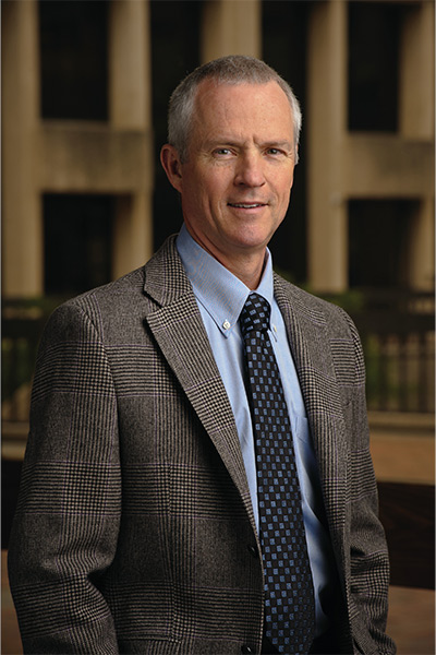 David Russell, Ph.D man wearing brown tweed suit against library background