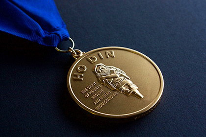 Gold medal on a chain laying on a field of navy blue.