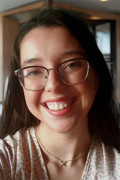 Smiling woman with long dark hair, wearing a light-color top and glasses.