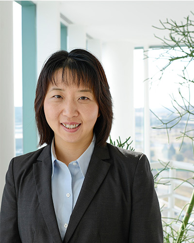 Yang Xie, Ph.D. woman in dark suit, white background, green plant