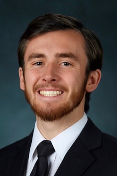 Smiling man with brown hair, beard, and mustache, wearing a dark suit and tie.