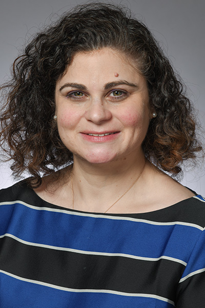 Smiling woman with dark curly hair wearing a blouse with blue and black stripes.