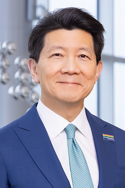 Smiling man with thick, dark hair wearing a blue suit and tie with a white dress shirt.