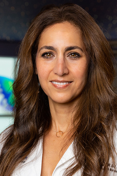 Smiling woman with long brown hair wearing a white lab coat.
