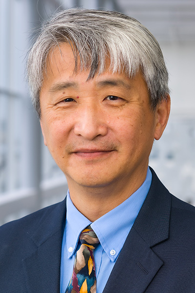 Smiling man with gray hair wearing a navy-blue suit over a light blue shirt with a multi-color tie.
