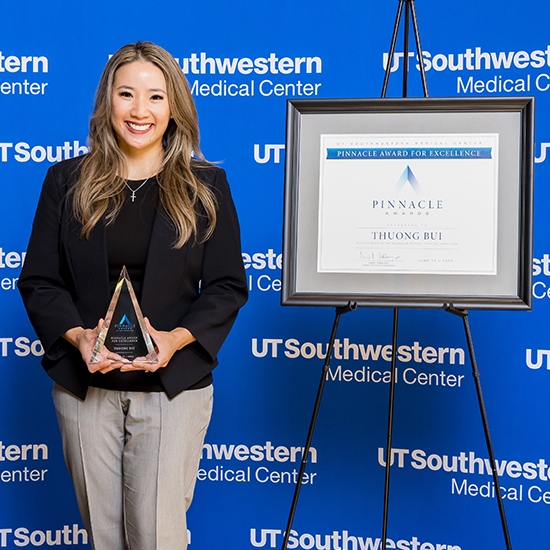 Pinnacle Awards Excellence recipient poses with her award and certificate against the blue UT Southwestern Medical Center wall.