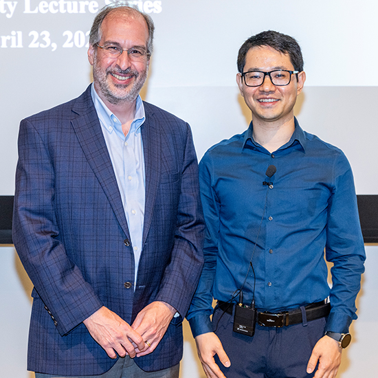 Two smiling men with glasses, wearing business casual attire.