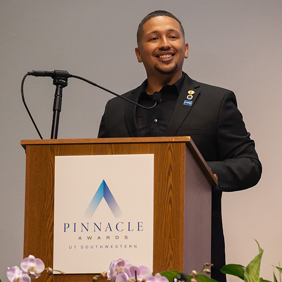 A speaker at the Pinnacle Awards UT Southwestern pedistal smiles at the unseen audience.