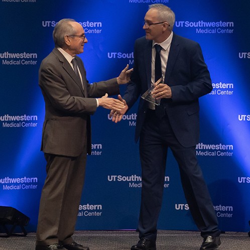 An awardee recieves his award and a handshake on stage