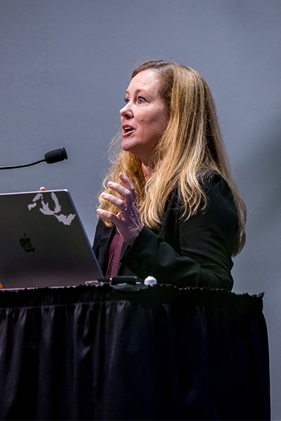 Ondine Cleaver Woman with long blond hair, speaks from a podium.