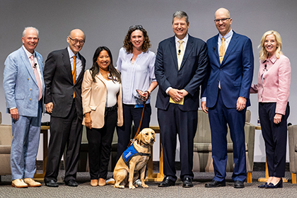 Six people gather onstage with the poster winner and a golden retriever.