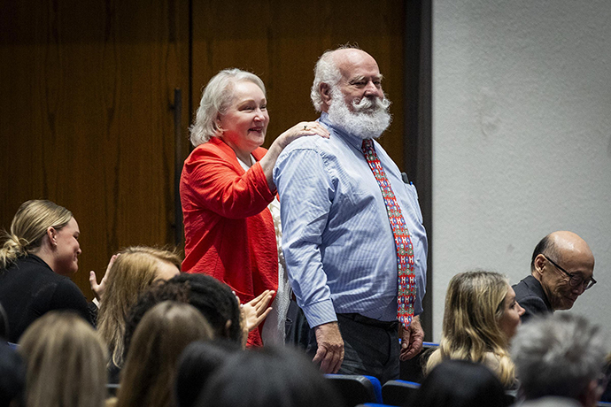 Mr. and Mrs. Rassmusen in the audience. A woman with blond hair and a man with a full white beard stand amid an audience.
