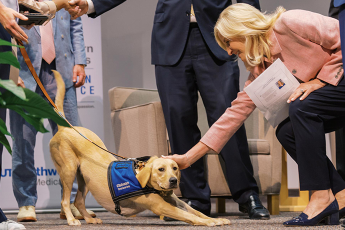 Tia and Susan Hernandez Woman with blond hair, bends over to pet a beautiful golden dog.