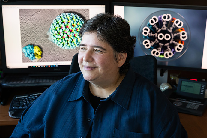 Dr. Nicastro Woman with dark hair, wearing a blue jacket, seated in front of two computer monitors displaying scientific objects.