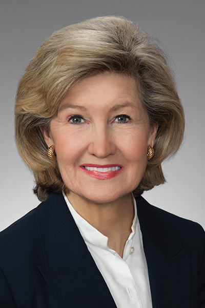 Kay Bailey Hutchison Smiling woman with blond hair, wearing a black jacket over a white blouse.