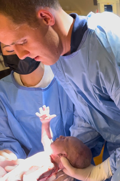 doctor in blue scrubs holds newborn son