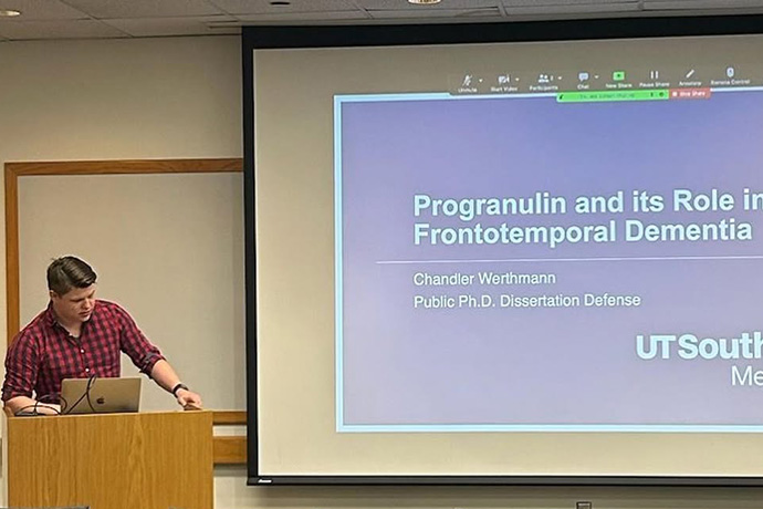 young man at podium presents research slides